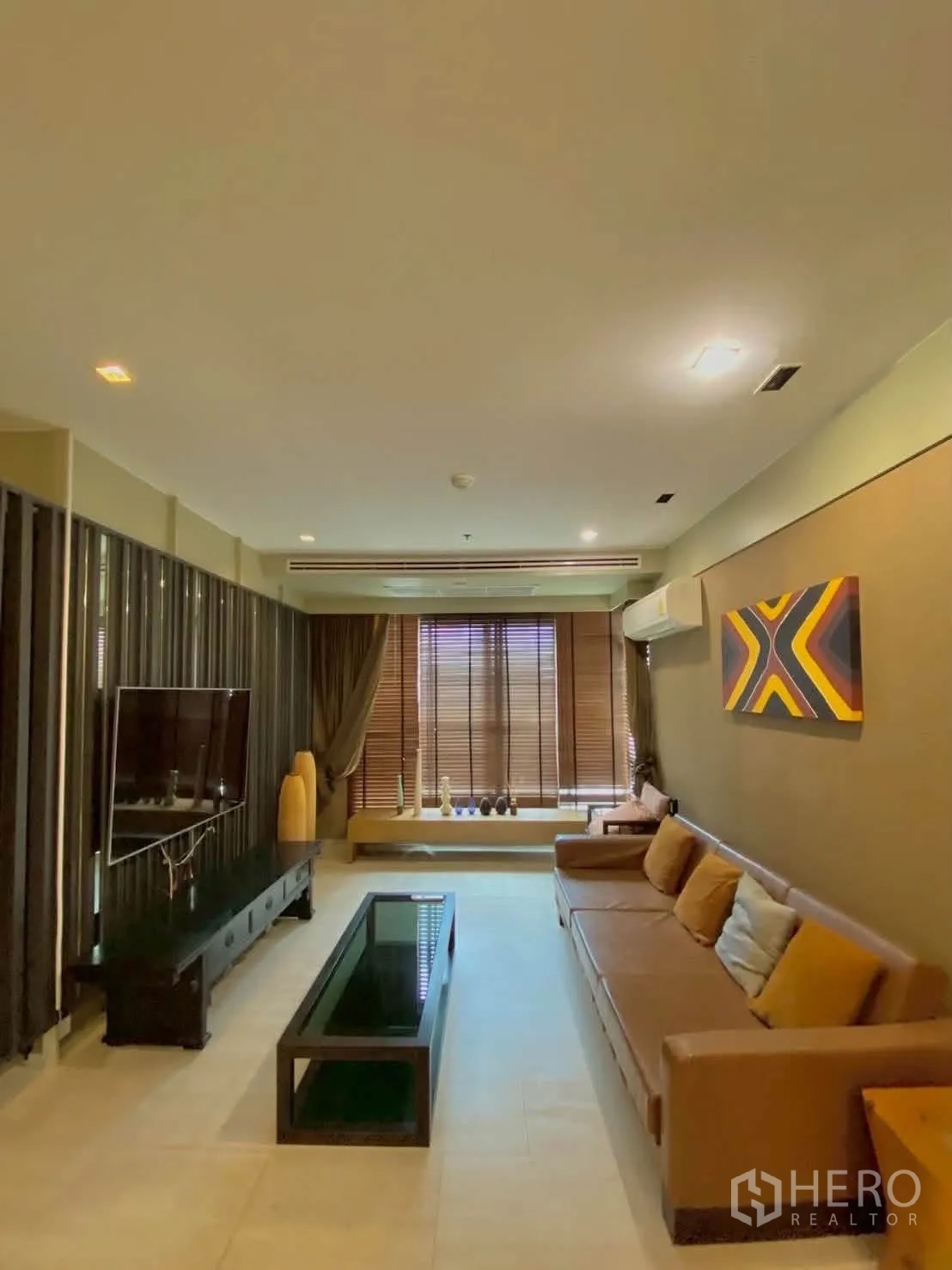 公寓 for rent in Khlong Toei, Bangkok - 客厅配棕色沙发、墙挂电视与木质百叶帘。