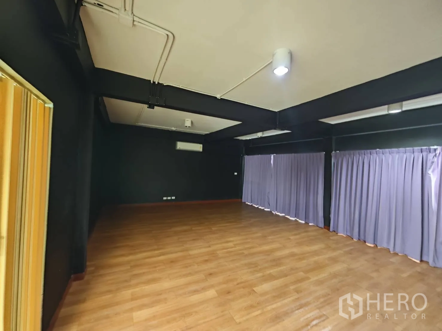 Office Space for rent in Prawet, Bangkok - Dark studio-style room with wood floors, black walls and blackout curtains.