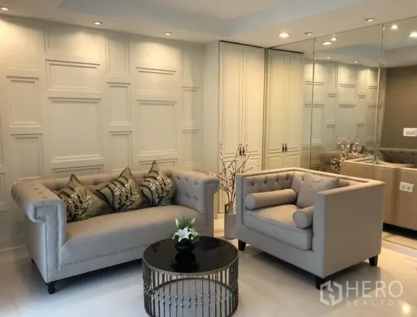 公寓 出租或出售在Sathon, Bangkok - 客厅配纽扣靠背沙发与扶手椅，镜面墙和圆形茶几，筒灯照明。