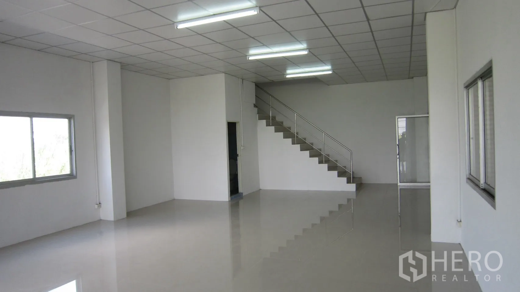 Warehouse for rent in Bang Sao Thong, Samut Prakan - Ground-floor office area with staircase, windows and fluorescent lighting inside the warehouse.