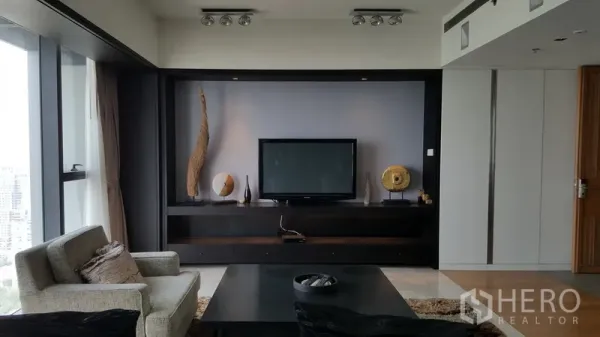 Condominium for rent in Sathon, Bangkok - Feature wall with mounted TV, display shelving, and seating area beside floor-to-ceiling windows.