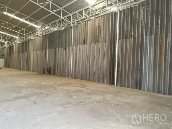 Warehouse for rent in Min Buri, Bangkok - Spacious warehouse interior with concrete floor, high steel trusses and corrugated metal wall.