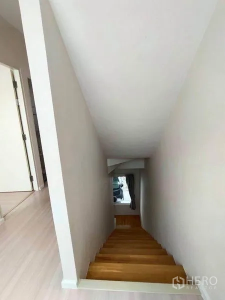 联排别墅 出租在Wang Thonglang, Bangkok - 从楼上向下的木质楼梯，白色墙面与自然采光。