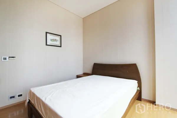 公寓 出售在Bang Rak, Bangkok - 明亮卧室，木质床架与浅色墙面，挂画装饰的曼谷公寓空间。