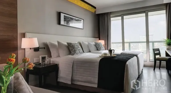 อพาร์ทเมนท์ ให้เช่าในKhlong San, Bangkok - ห้องนอนเตียงคู่ โคมไฟหัวเตียง และโต๊ะทำงาน มองเห็นวิวเมืองผ่านประตูกระจกบานเลื่อน