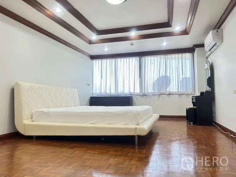 Condominium for sale in Huai Khwang, Bangkok - Expansive bedroom featuring a king bed, parquet floors, coffered ceiling, and air conditioning.