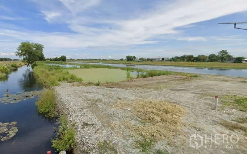 Land for sale in Chachoengsao - Gravel clearing beside canals and ponds under a blue sky in rural Chachoengsao.