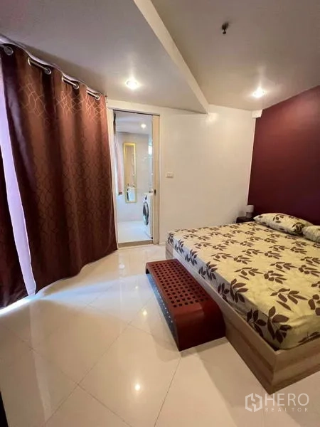 Condominium for rent in Ratchathewi, Bangkok - Cozy bedroom with patterned bedding, blackout curtains, and ensuite access.