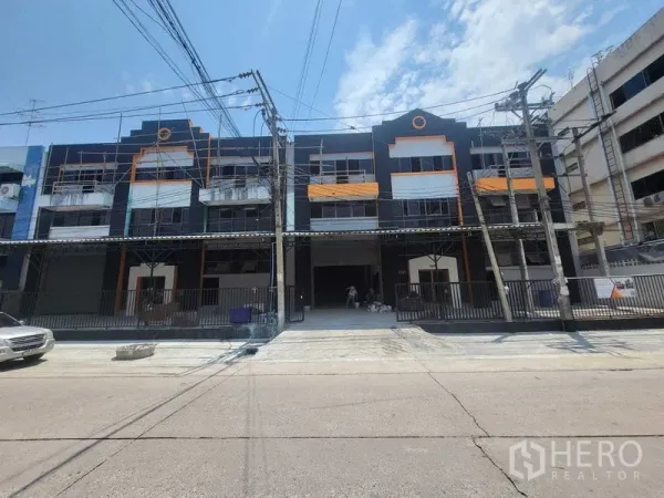 工厂 出租或出售在Samut Prakan - 工业楼正立面，黑橙配色，带车道与大门。