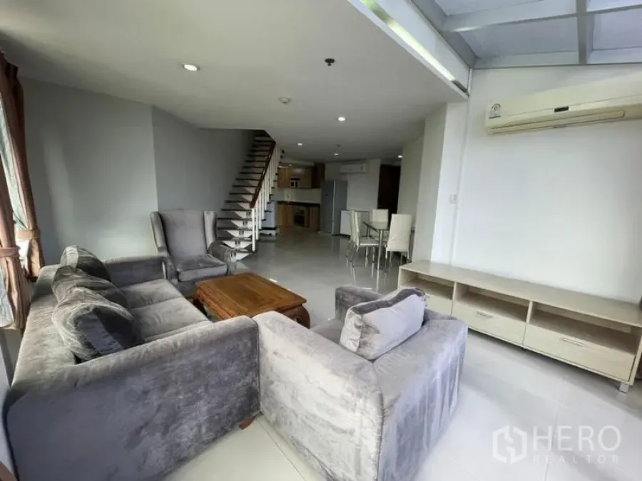 คอนโด ให้เช่าในKhlong Toei, Bangkok - ห้องนั่งเล่นคอนโดโปร่งสว่างในคลองเตย โซฟาสีเทา โต๊ะไม้ บันไดภายใน พื้นที่รับประทานอาหารและครัว ใกล้ BTS พร้อมพงษ์