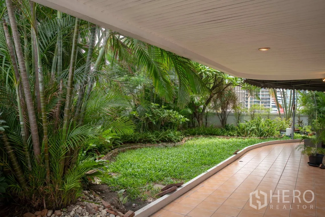 Apartment for rent in Khlong Toei, Bangkok - Lush landscaped garden with palms and a curved walkway under the canopy.