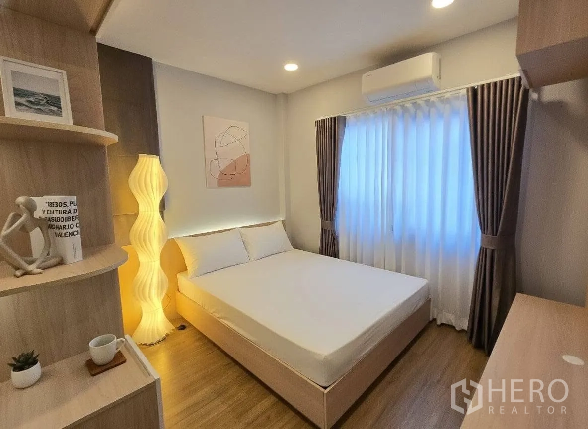 Detached House for rent or sale in Bang Phli, Samut Prakan - Cozy bedroom with double bed, warm floor lamp, built‑in shelves, curtains and wood flooring.