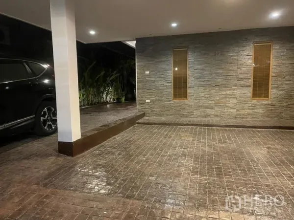 ทาวน์เฮาส์ ให้เช่าในSuan Luang, Bangkok - พื้นที่จอดรถในร่ม ผนังกรุหิน พื้นทางรถเข้าลายอิฐ พร้อมไฟดาวน์ไลท์และต้นไม้ริมทาง