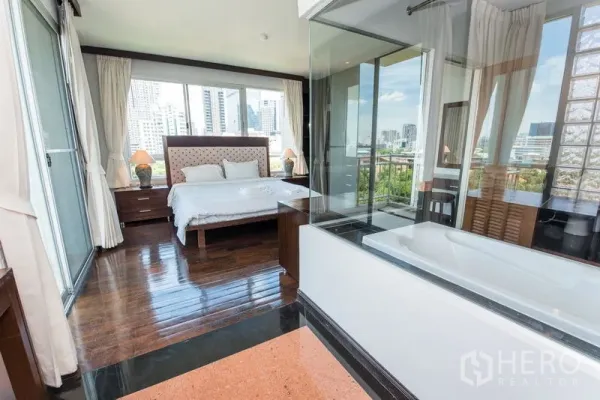 Condominium for rent in Sathon, Bangkok - Master bedroom with hardwood floors and a glass-walled bathroom featuring a bathtub and skyline view.