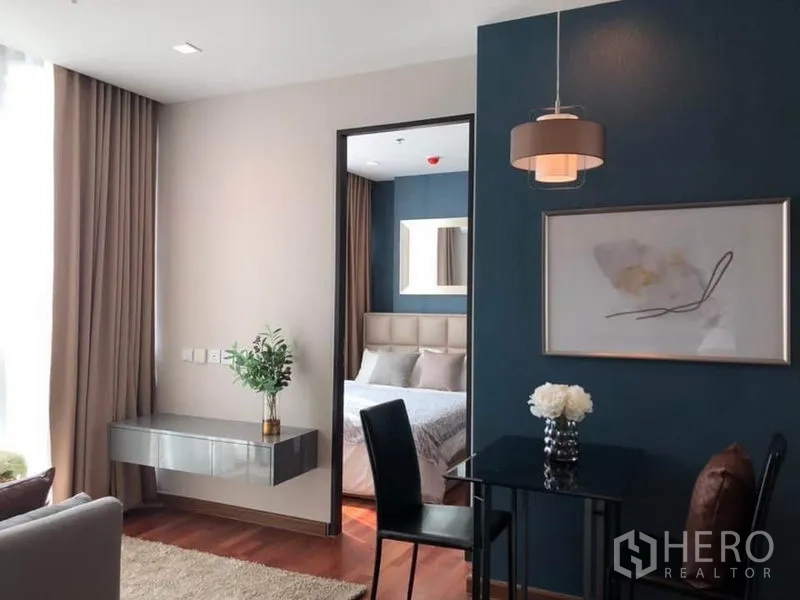 Condominium for rent or sale in Ratchathewi, Bangkok - Living space with tall curtains, floating console shelf, doorway to bedroom, and dining table.