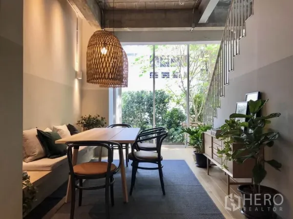 Townhouse for rent in Khlong Toei, Bangkok - Bright dining area with built-in bench, rattan pendant light and floor-to-ceiling glass opening to a garden.