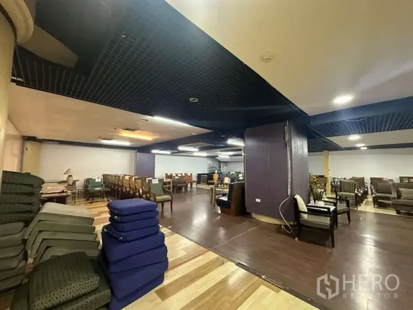 零售空间 出租 - 零售铺面角落，堆放坐垫、立柱与多组座椅，双色木地板。