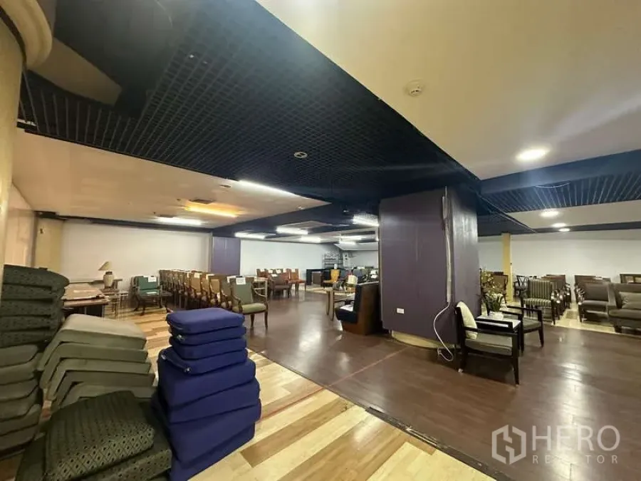 零售空间 出租 - 零售铺面角落，堆放坐垫、立柱与多组座椅，双色木地板。