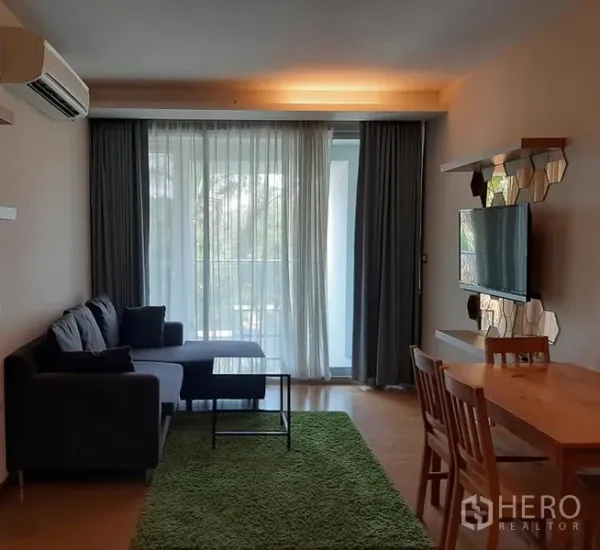 Condominium for sale in Watthana, Bangkok - Bright living and dining area with sofa, TV wall, and balcony behind sheer curtains in a modern Watthana condo.