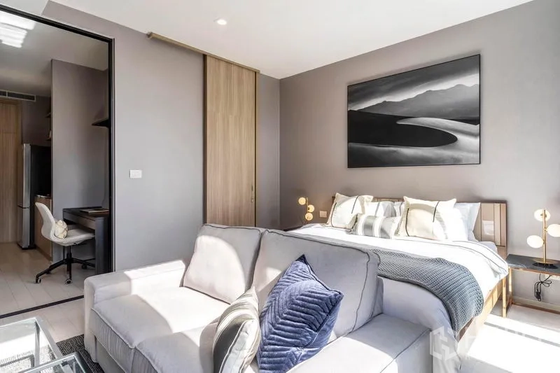 คอนโด ให้เช่าในPathum Wan, Bangkok - ห้องนอนมีโซฟาวางปลายเตียง งานศิลป์ผนัง และโคมไฟหัวเตียงแสงอบอุ่น