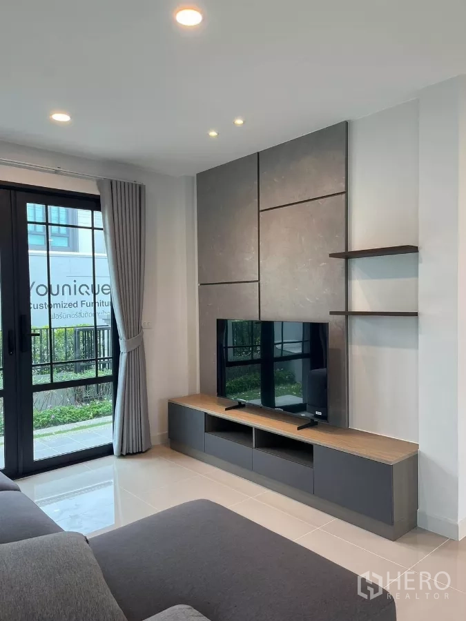 Detached House for rent or sale in Bang Phli, Samut Prakan - Media wall with shelving and TV unit beside sliding glass doors and full curtains.