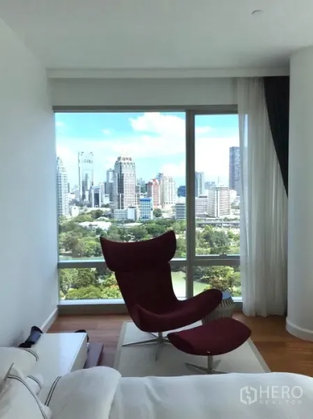Condominium for rent or sale in Pathum Wan, Bangkok - Bedroom corner with red lounge chair and panoramic Lumpini Park skyline view