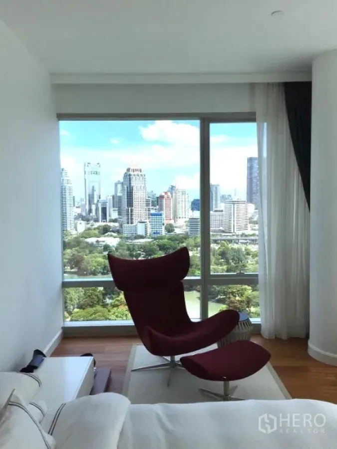 Condominium for rent or sale in Pathum Wan, Bangkok - Bedroom corner with red lounge chair and panoramic Lumpini Park skyline view