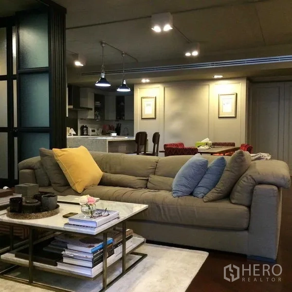 Condominium for sale in Pathum Wan, Bangkok - Cozy lounge with plush sectional sofa, coffee table and pendant lighting facing the kitchen.