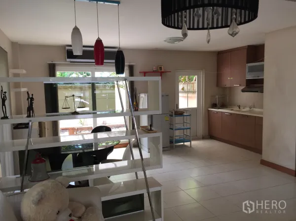 Townhouse for rent or sale in Bueng Kum, Bangkok - Open-plan kitchen and dining area with pendant lights, white shelving divider and sliding glass doors to a patio.