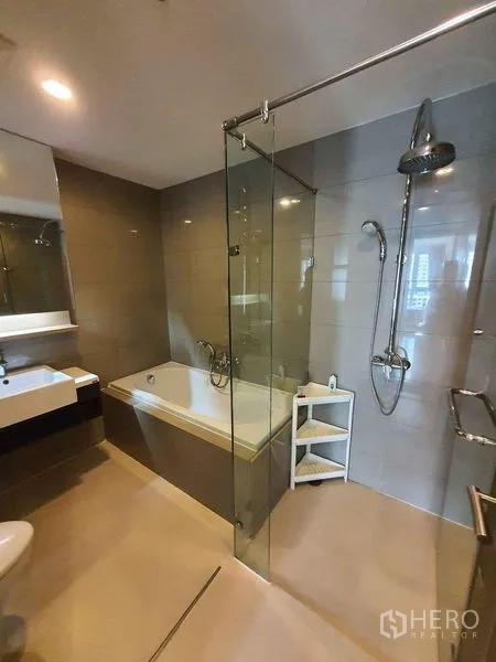 Condominium for rent in Watthana, Bangkok - Modern bathroom with glass shower, bathtub and vanity in neutral tiles.