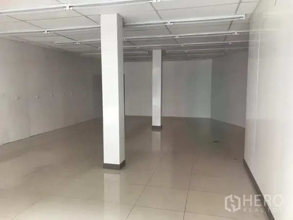 零售空间 出租在Khlong Toei, Bangkok - 一层空置零售铺面，白色墙面、亮面地砖、承重柱及带荧光灯轨道的吊顶。