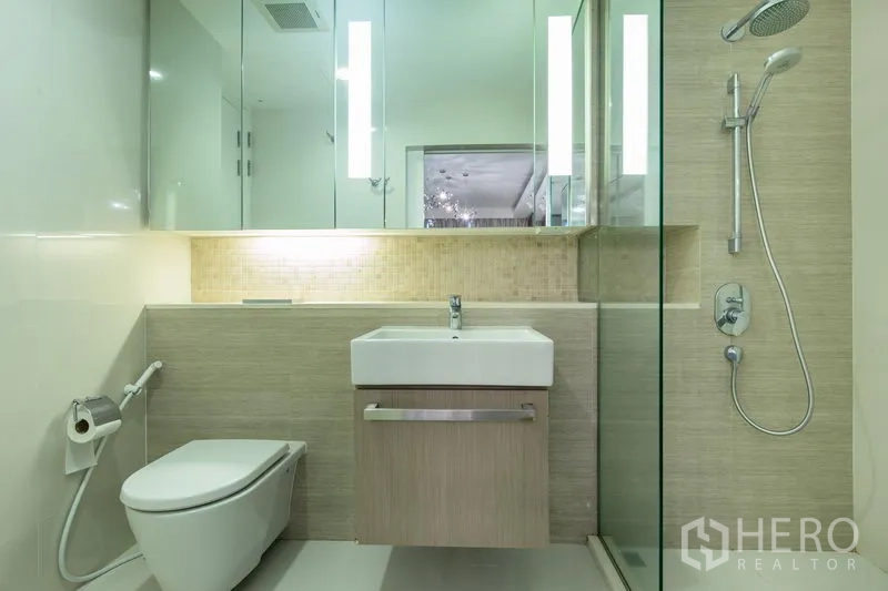 公寓 出租在Watthana, Bangkok - 简约浴室，玻璃淋浴间、挂墙式马桶、台盆与背光镜。