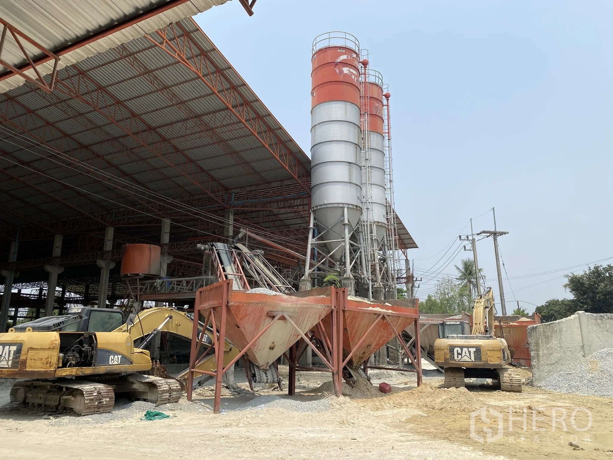 Factory for sale in Mueang Chon Buri, Chon Buri - Equipment yard with hoppers, excavators and silos beside covered plant.