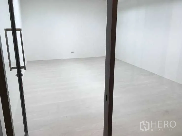 Office Space for rent in Pak Kret, Nonthaburi - Bright empty office room with light wood flooring viewed through a glass door.