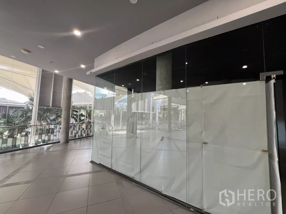 零售空间 出租 - 转角玻璃店面朝向中庭步道，可见顶棚与棕榈树景观。