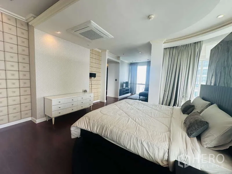 คอนโด ให้เช่าหรือขายในKhlong Toei, Bangkok - ห้องนอนมาสเตอร์กว้าง เตียงคิงส์บนแท่นโค้ง มุมพักผ่อน และพื้นไม้สีเข้มใกล้หน้าต่างสูง