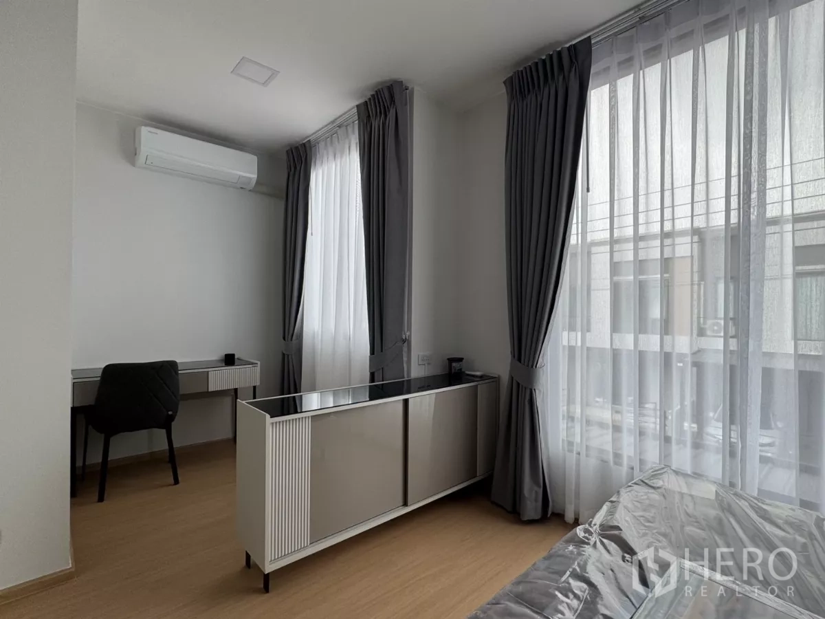 Townhouse for rent in Bang Phli, Samut Prakan - Corner bedroom with study desk and wraparound windows with curtains.