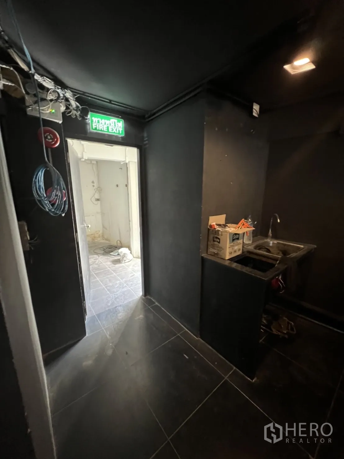 Home Office for rent or sale in Khlong Toei, Bangkok - Back-of-house corridor with small sink, exposed wiring and fire exit sign.