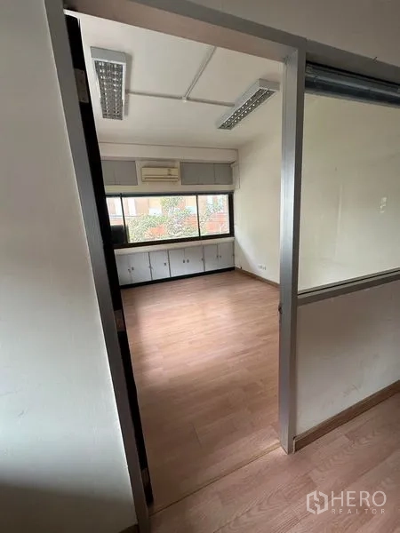 Office Space for rent in Khlong Toei, Bangkok - Compact private office with wood flooring, a window, and built-in storage cabinets.