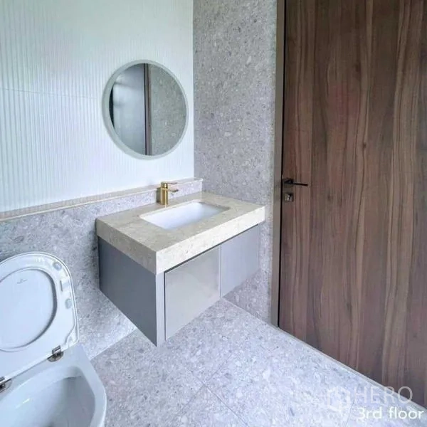 Detached House for rent in Bang Kapi, Bangkok - Guest bathroom with round mirror and stone vanity beside wooden door.