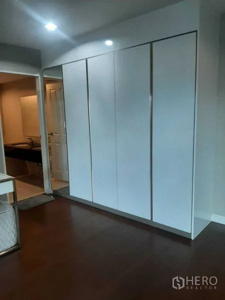Condominium for rent or sale in Huai Khwang, Bangkok - Built-in white wardrobes along a bedroom wall with wood flooring.