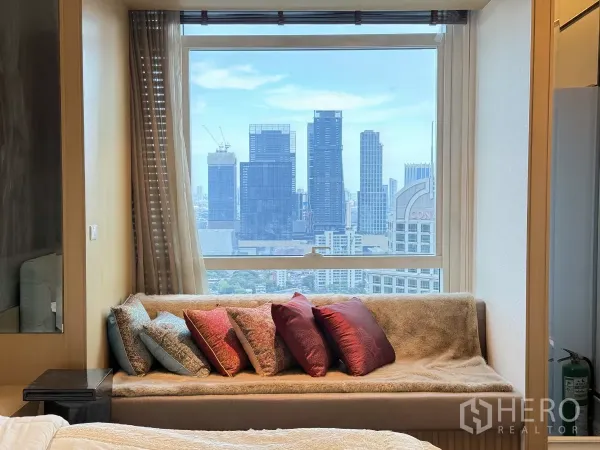 คอนโด ให้เช่าในPathum Wan, Bangkok - ม้านั่งริมหน้าต่างในห้องนอนพร้อมหมอนสีสัน มองเห็นตึกสูงในกรุงเทพฯ