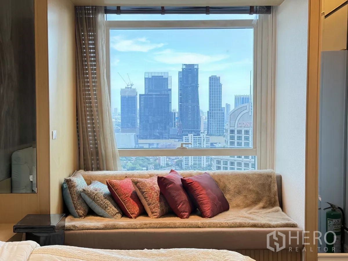 คอนโด ให้เช่าในPathum Wan, Bangkok - ม้านั่งริมหน้าต่างในห้องนอนพร้อมหมอนสีสัน มองเห็นตึกสูงในกรุงเทพฯ