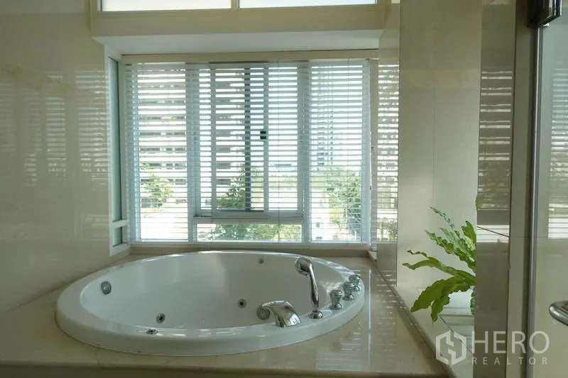Condominium for rent in Khlong Toei, Bangkok - Bathroom with round jacuzzi tub by a window with blinds and greenery.