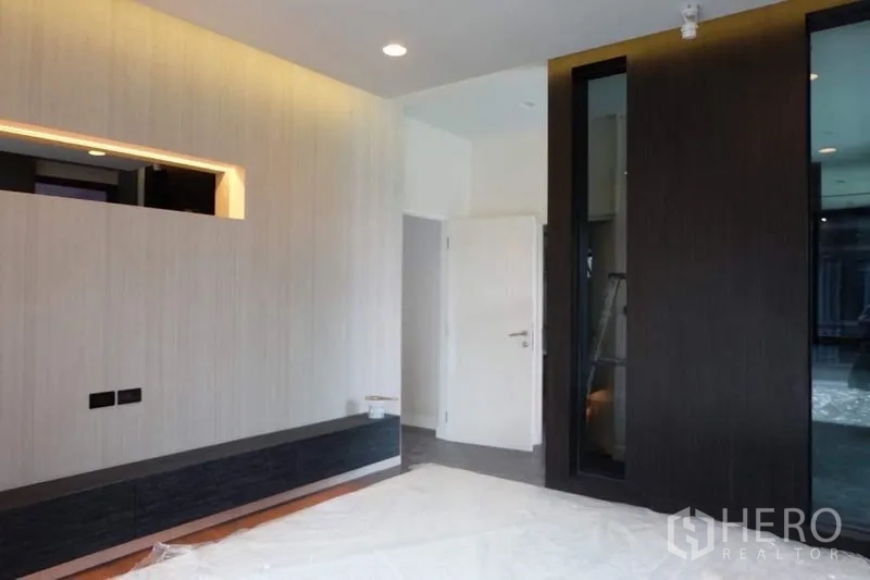 Detached House for rent in Bang Kapi, Bangkok - Bedroom angle showing light wood panel feature wall, dark cabinet and white interior door.
