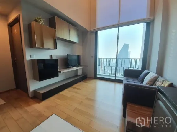 คอนโด ให้เช่าหรือขายในKhlong Toei, Bangkok - ห้องนั่งเล่นหน้าต่างสูงจรดเพดาน ผนังทีวีบิลท์อิน และประตูสไลด์สู่ระเบียง