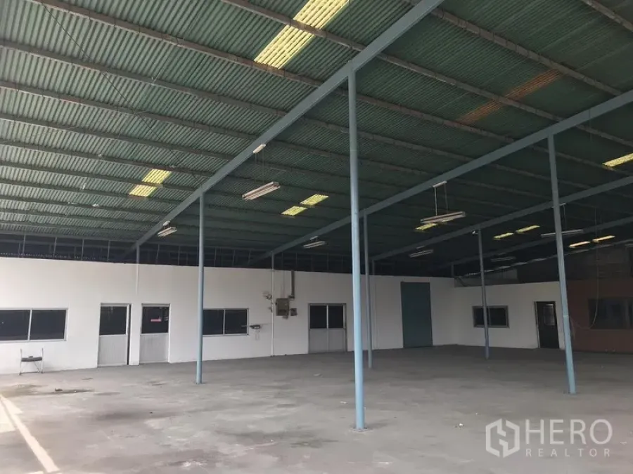 Warehouse for rent in Bang Phli, Samut Prakan - Open-plan warehouse interior with high steel roof, skylights, suspended lights, concrete floor, and partitioned offices.