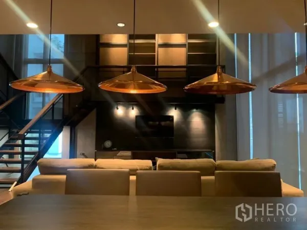 คอนโด ให้เช่าในWatthana, Bangkok - ห้องนั่งเล่นสไตล์ลอฟต์ โคมไฟสีทองแดงเหนือโต๊ะอาหาร โซฟาและผนังทีวี