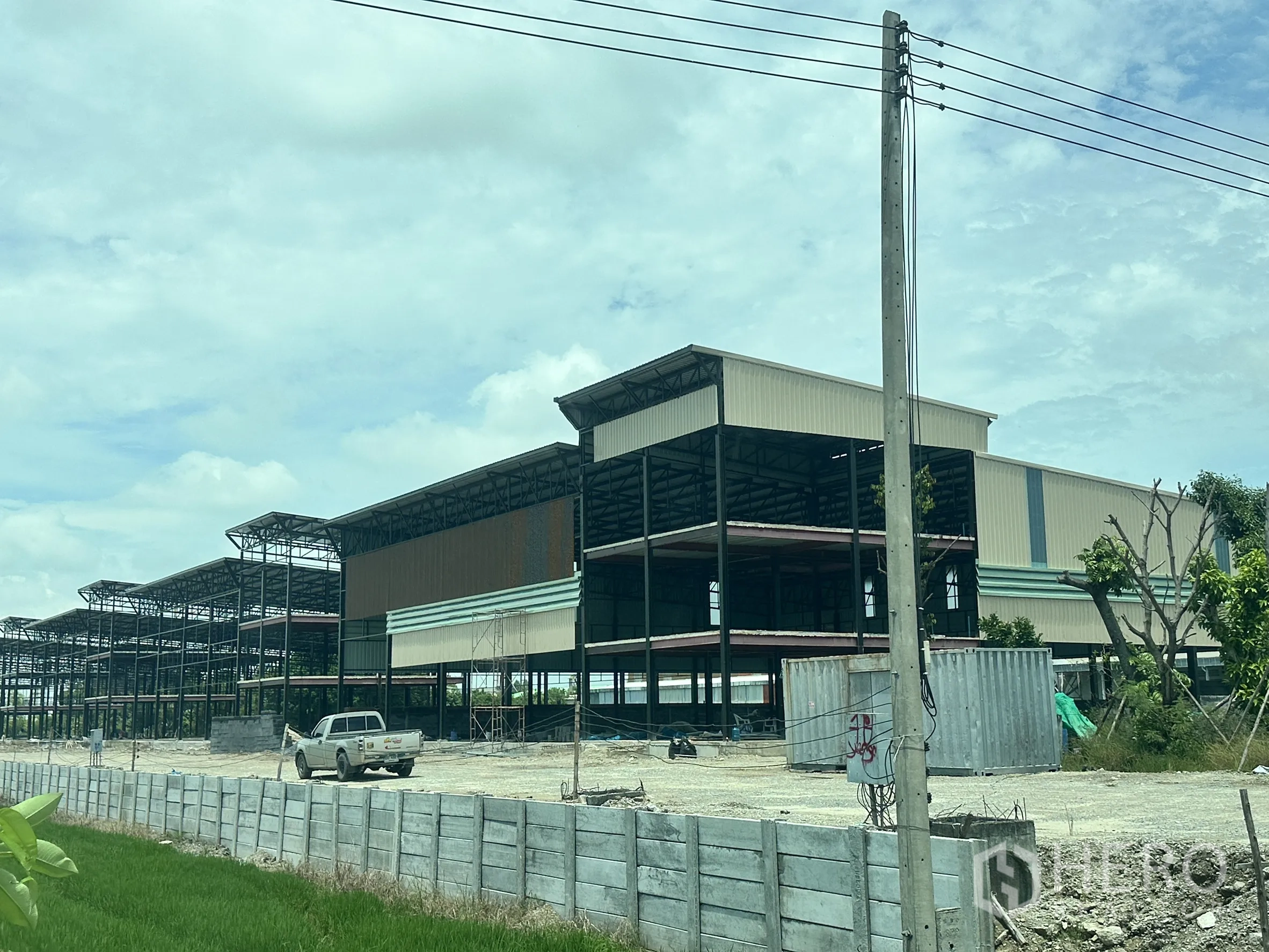 Warehouse for rent in Lam Luk Ka, Pathum Thani - Photo of a steel-frame warehouse under construction with multiple bays, a perimeter wall and open yard.