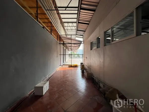 Warehouse for rent in Saphan Sung, Bangkok - Side corridor with tiled floor, ventilation awnings and chain-link gate beside the warehouse.